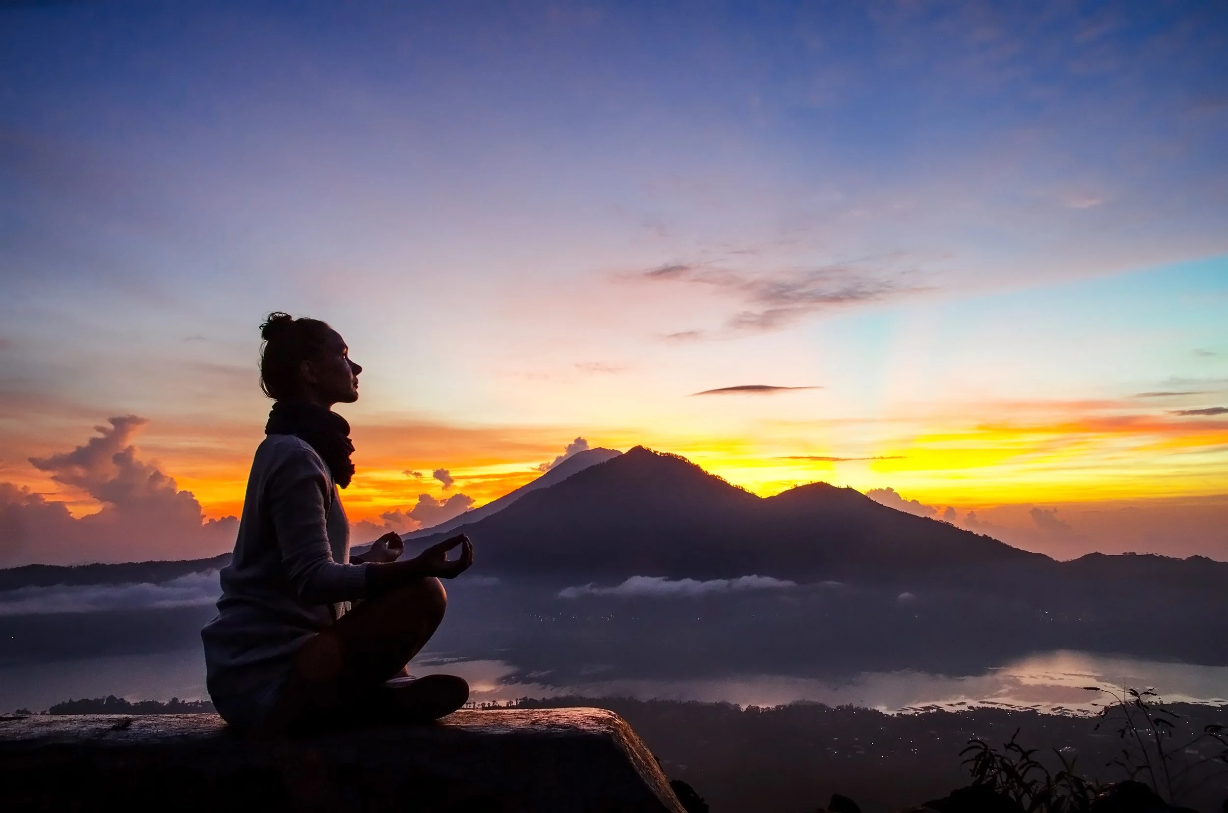 Woman meditating on with mountains in the background.