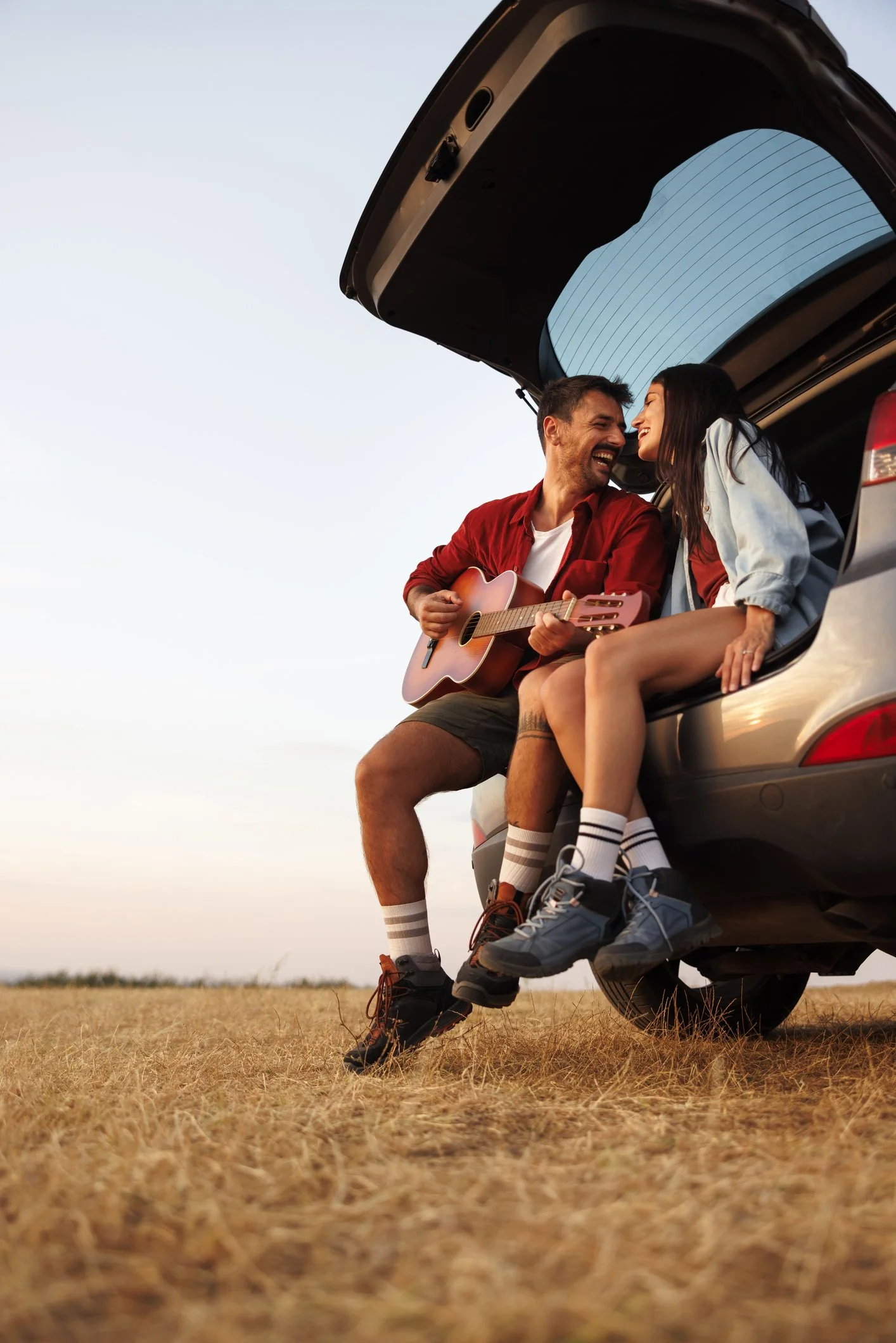 Young couple sitting in back of car playing guitar