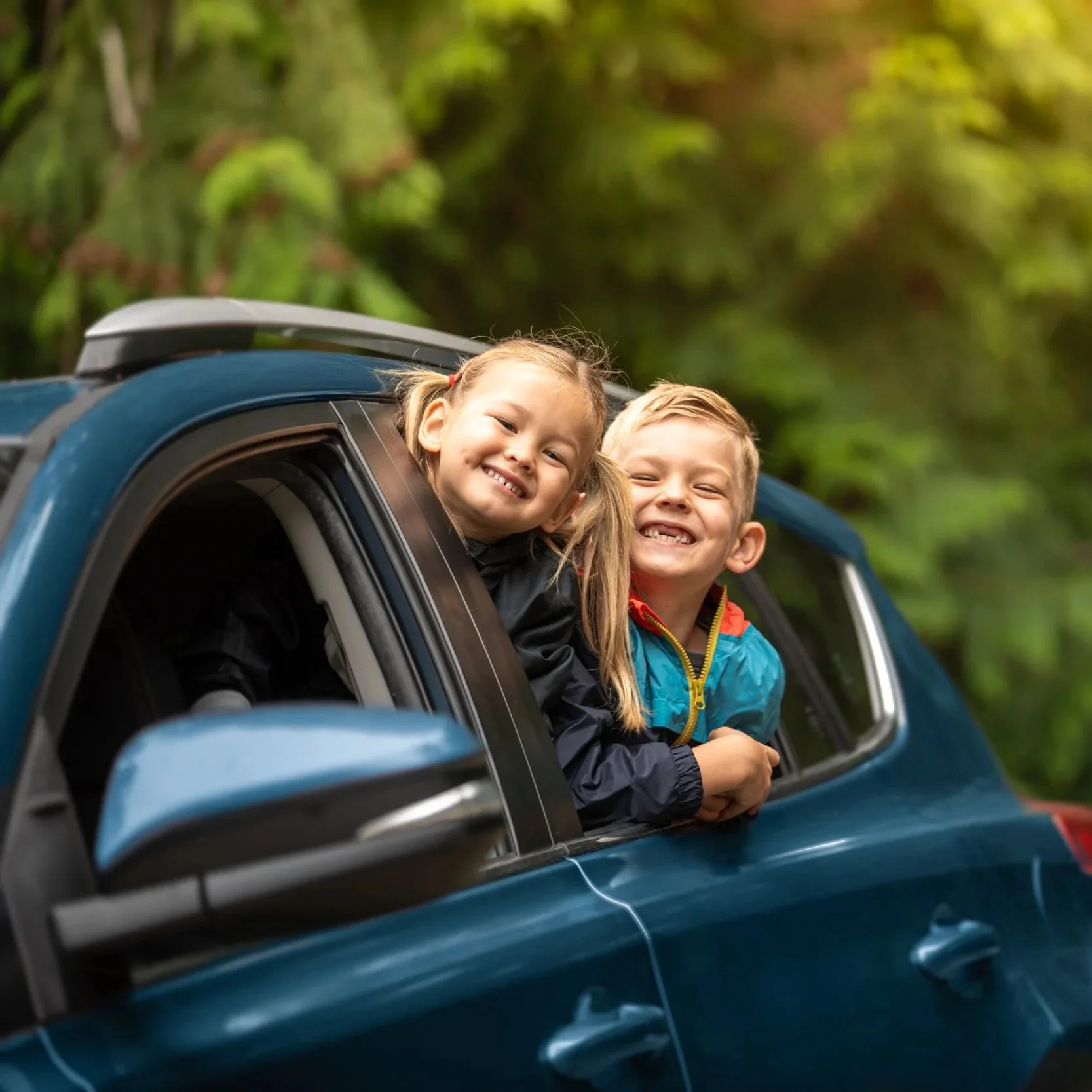 two smiling children sticking out of back seat window of car
