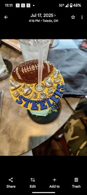 A hockey puck with the Pittsburgh Steelers logo, decorated with silver ice hockey game pucks around the edge, with a tall glass of drink on top.