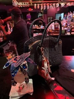 A jean handbag and decorative jean jewelry drink cover on a bar counter in a dimly lit bar or nightclub.