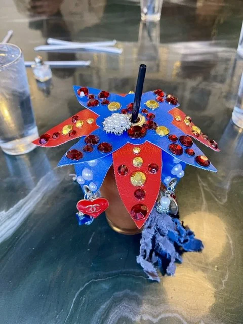 Colorful butterfly-shaped decoration with red, blue, yellow, and white accents, placed in a small container with a black straw in the center.
