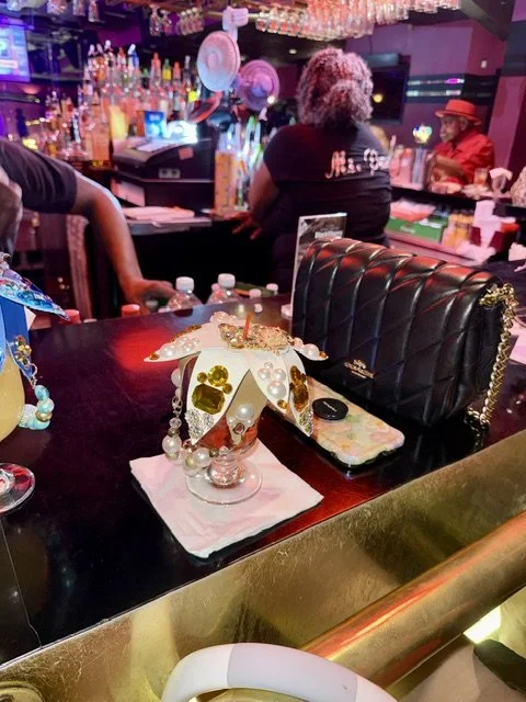 Decorative unicorn-themed cake on a bar counter in a lively, colorful bar with patrons and bottles in the background.