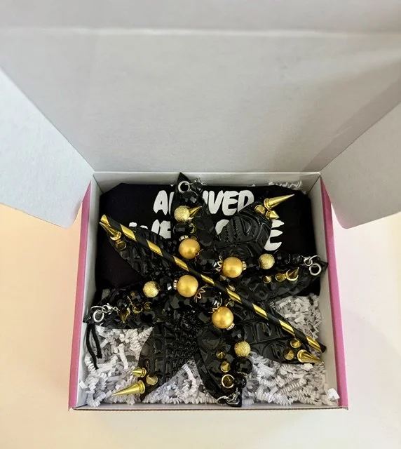 Open box containing black and gold jewelry, including earrings and a bracelet, with shredded paper filler.