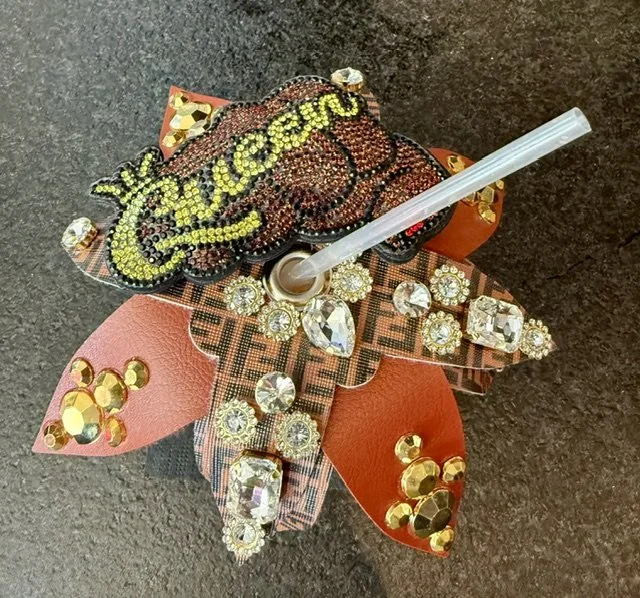 Decorative item with rhinestones and beads resembling a ladybug with the word 'chicome' on top, a straw inserted into the center.