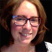 A woman with reddish hair and glasses smiles at the camera.