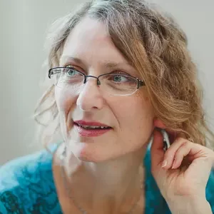 Woman with light brown hair with hand on ear 