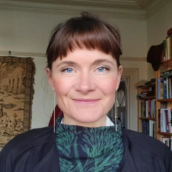 A white woman with brown hair and blue eyes smiles at the camera.