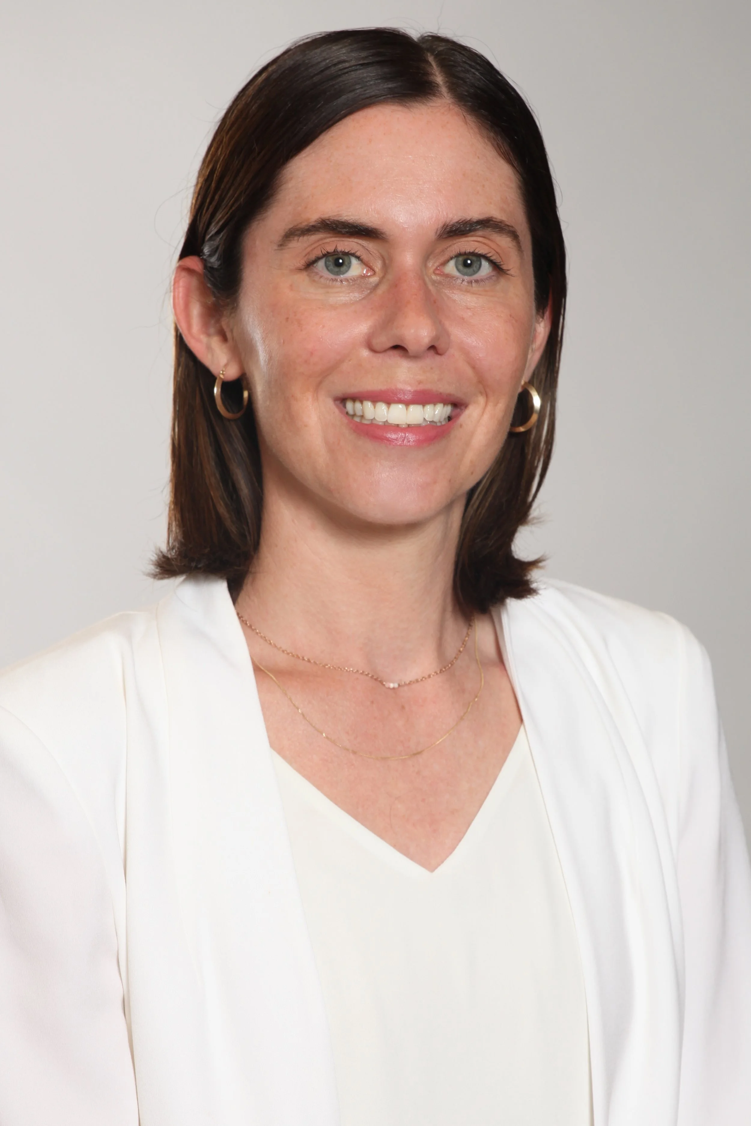 A white woman wearing a white shirt smiles for a professional headshot.