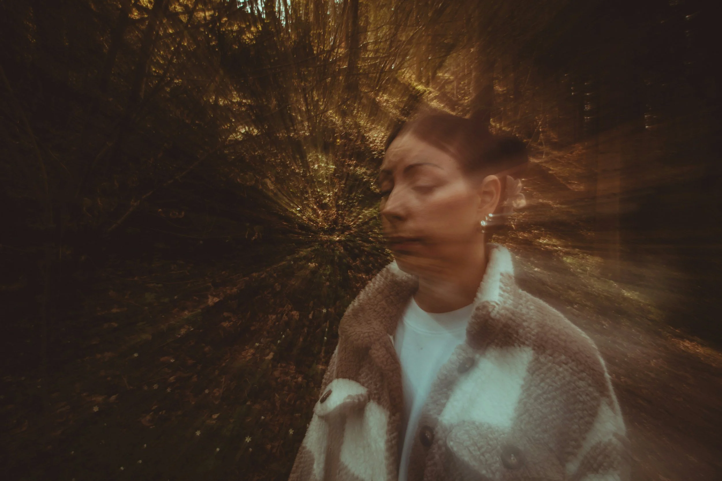 A woman with her eyes closed walking through a wooded area at night, illuminated by soft, warm light.