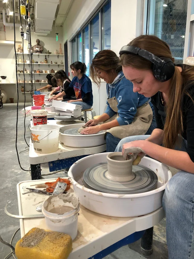 A row of students at the electric wheel in Karl McDade's ceramics class.