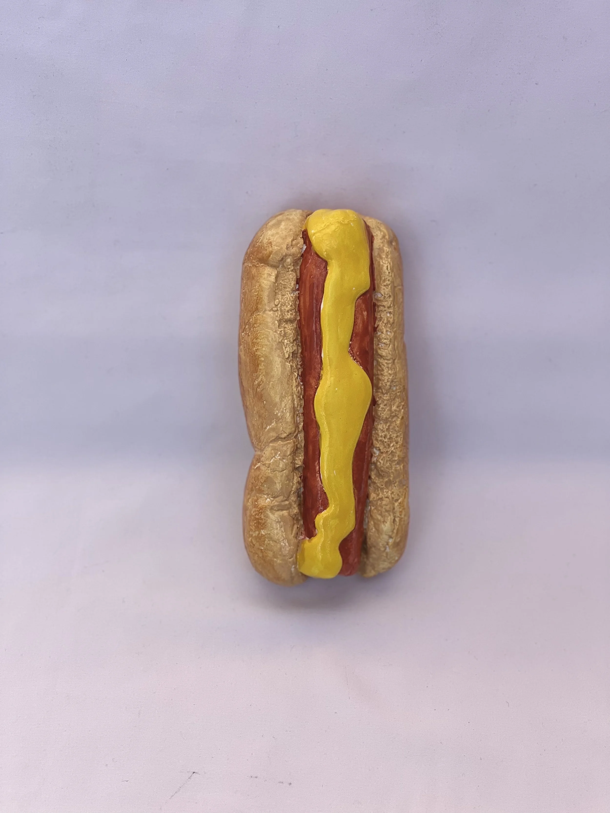 Realistically painted ceramic hot dog featuring mustard on a toasted bun created during a Ceramics on Wheels arts and crafts activity.