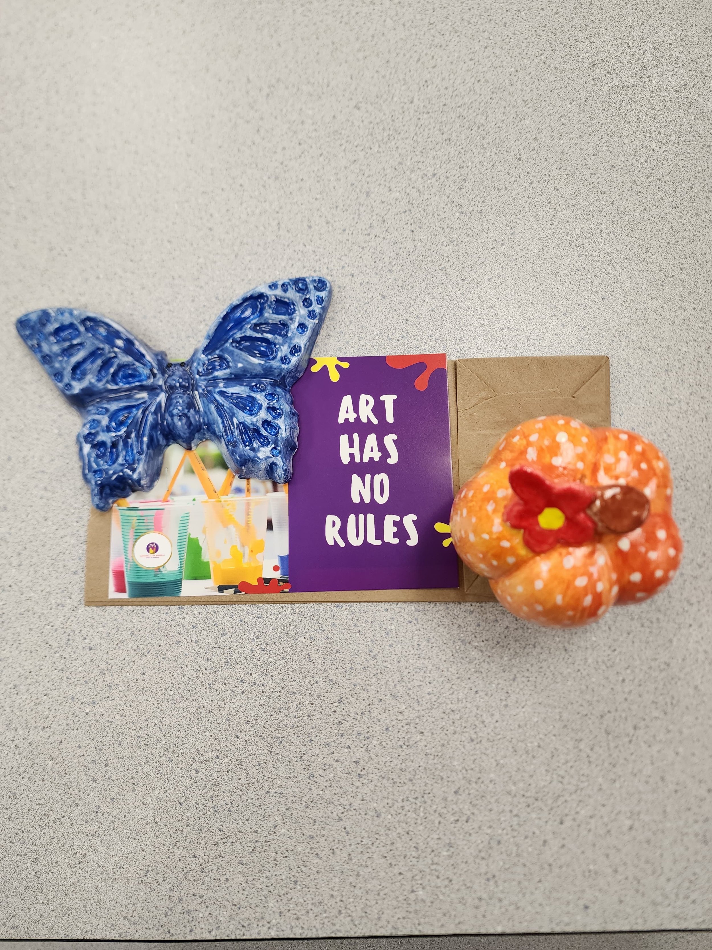 blue butterfly plaster art craft and a orange polka dot ceramic witha red flower and yeloow center pictured with a ceramics on wheels post card saying art has no rules