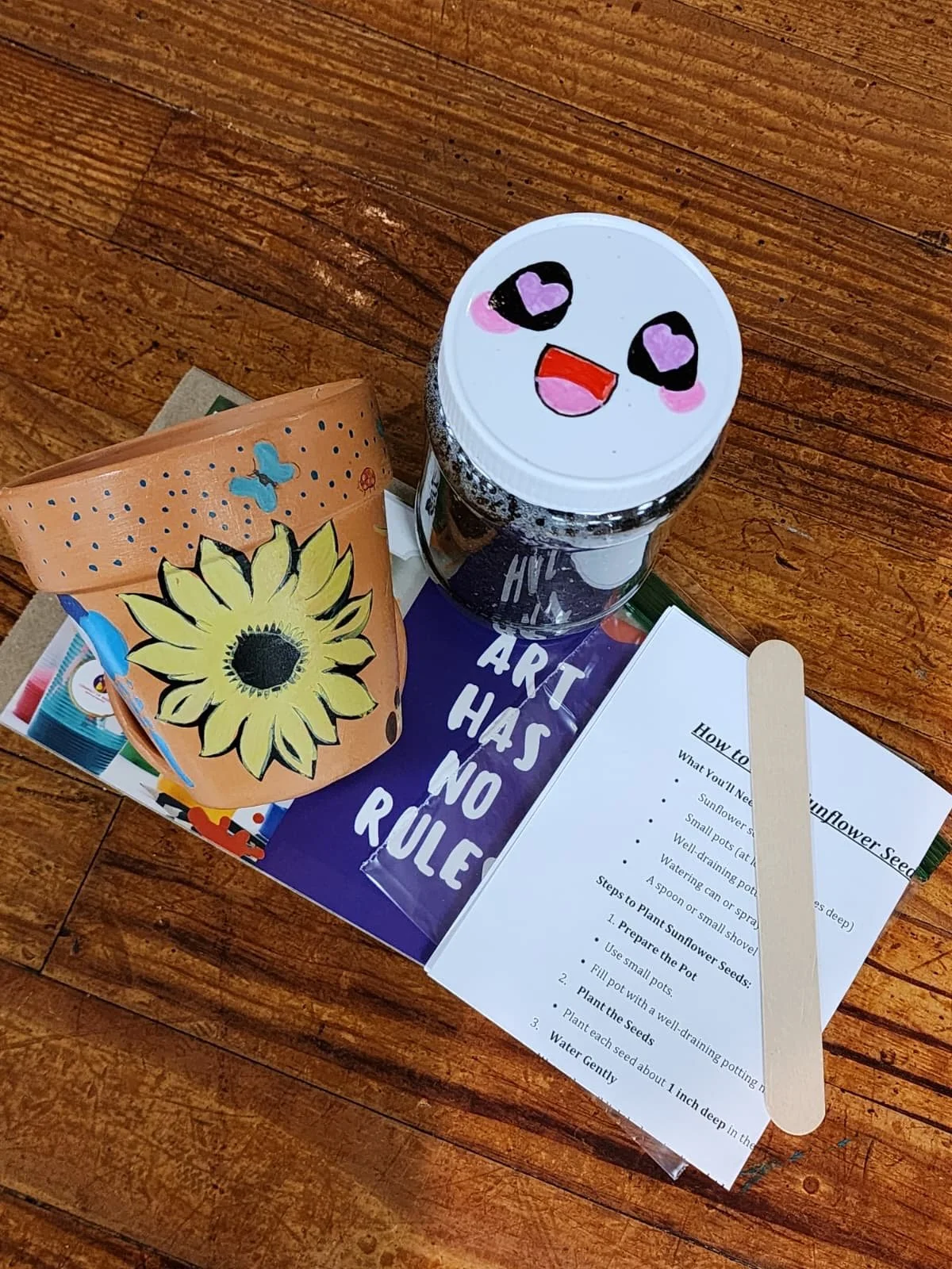TEAM art project featuring a flower pot painted with a yellow sunflower, along with sunflower seeds and soil for a hands-on grow-your-own sunflower activity.