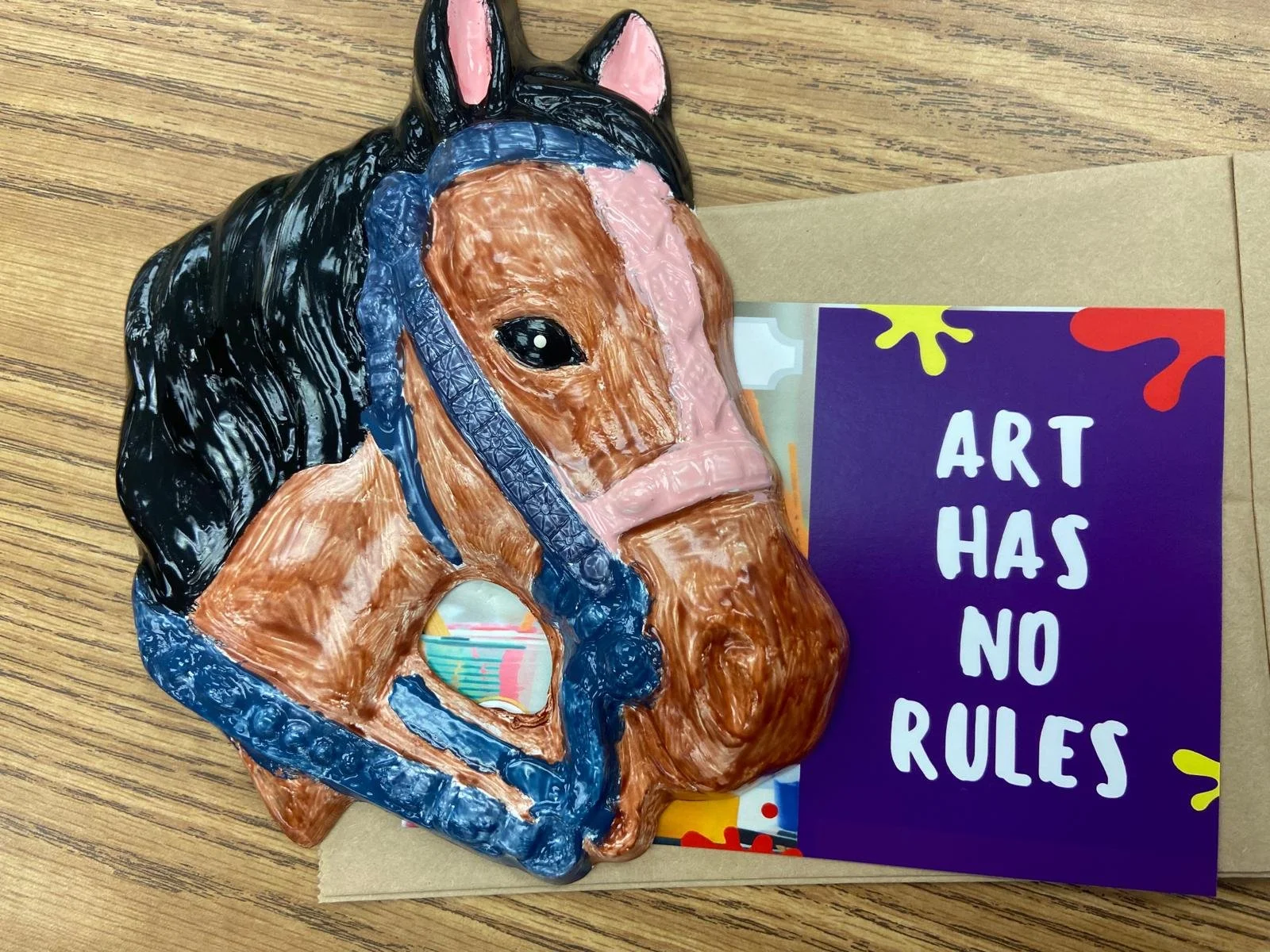 Hand-painted ceramic horse with a brown coat, black mane, pink ears, and blue muzzle created during a Ceramics on Wheels mobile arts and crafts workshop.