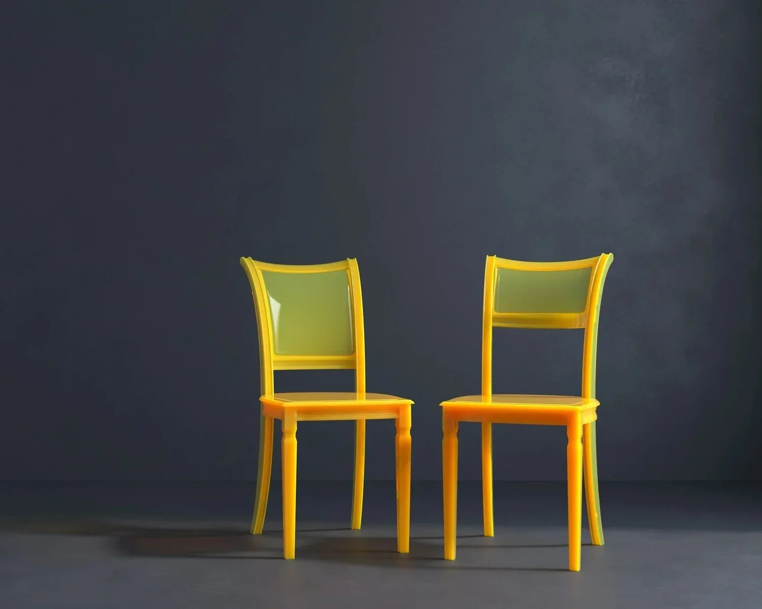 Two bright yellow chairs are placed on a dark gray background. The chairs are modern in design, creating a vibrant contrast with the subdued backdrop.