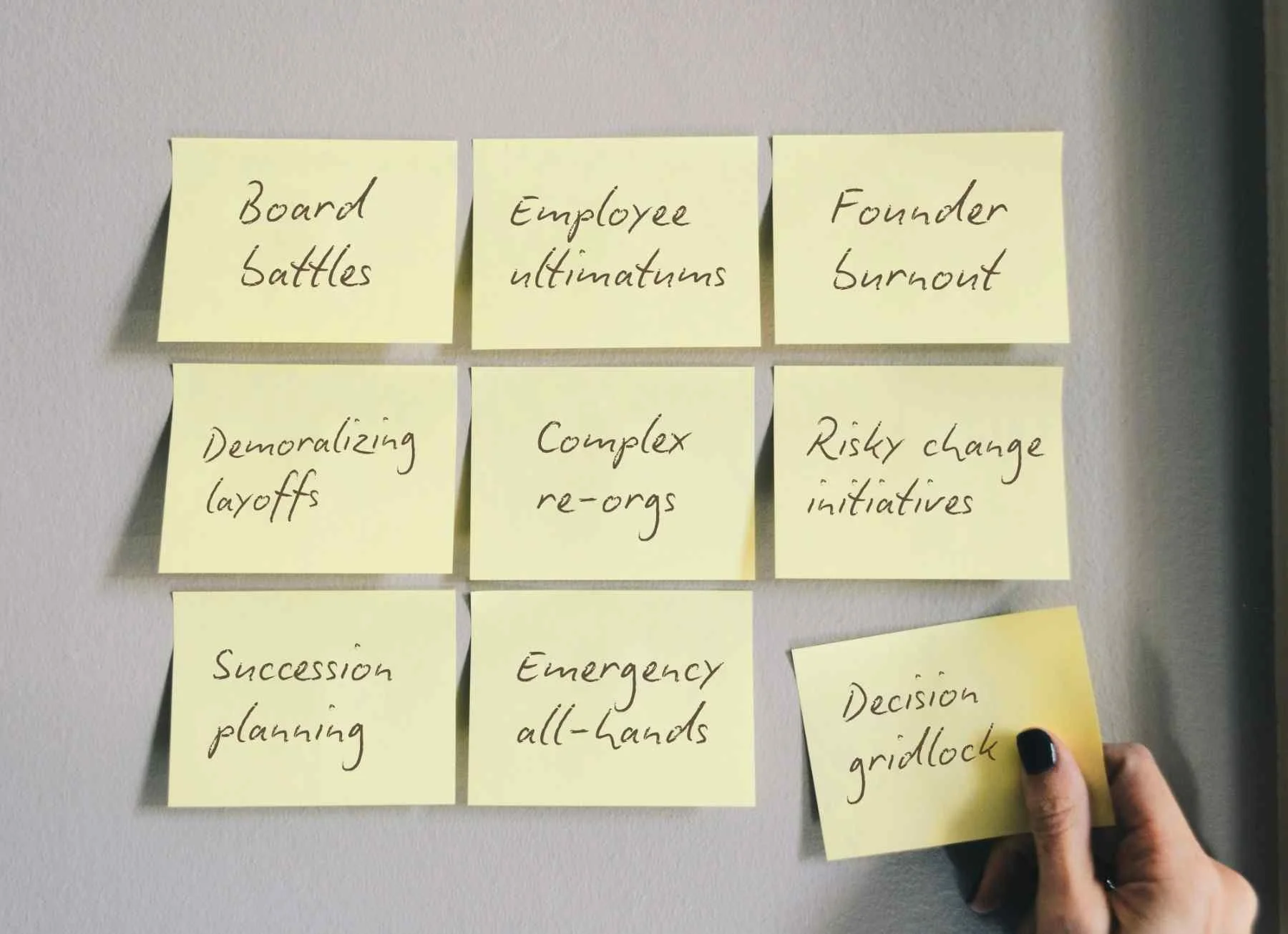 Nine yellow sticky notes on a wall list business challenges, like "Founder Burnout" and "Complex Re-orgs." A hand holds "Decision Gridlock" off to the side.