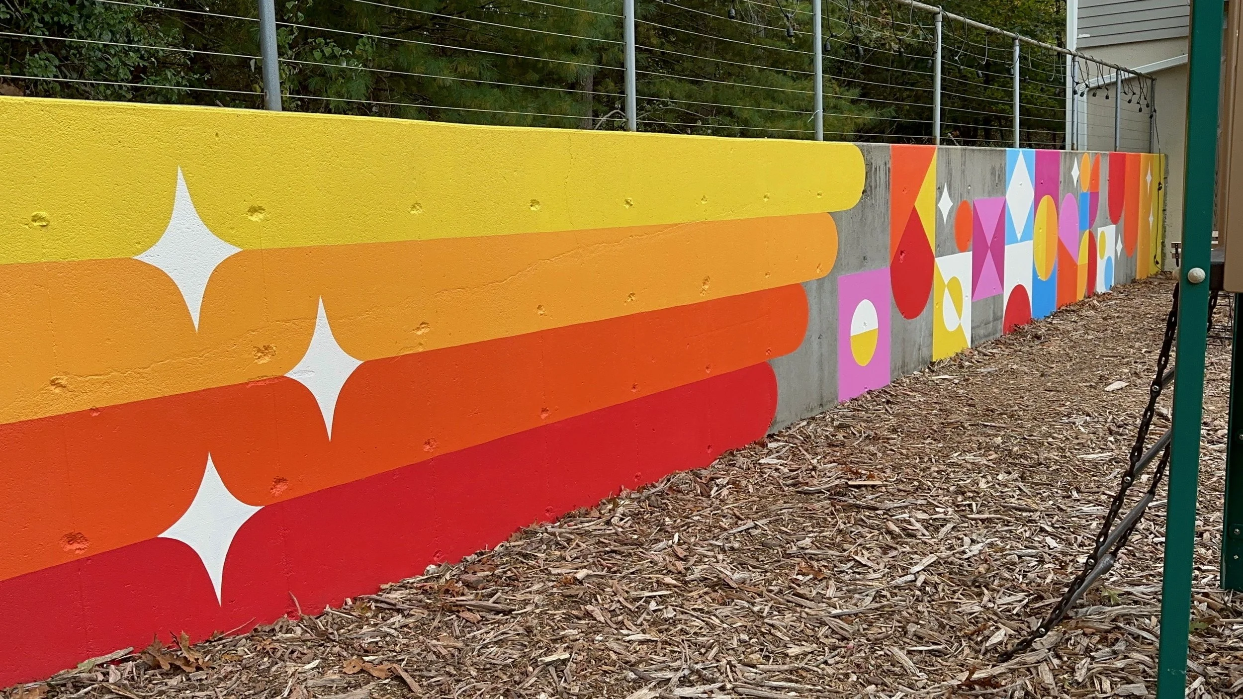 SHINE Studio Retaining Wall: a bright, geometric installation transformed this concrete retaining wall to a cheerful backdrop to the outdoor seating and playground areas.  One of a number of mural installations commissioned by the Studio of local art