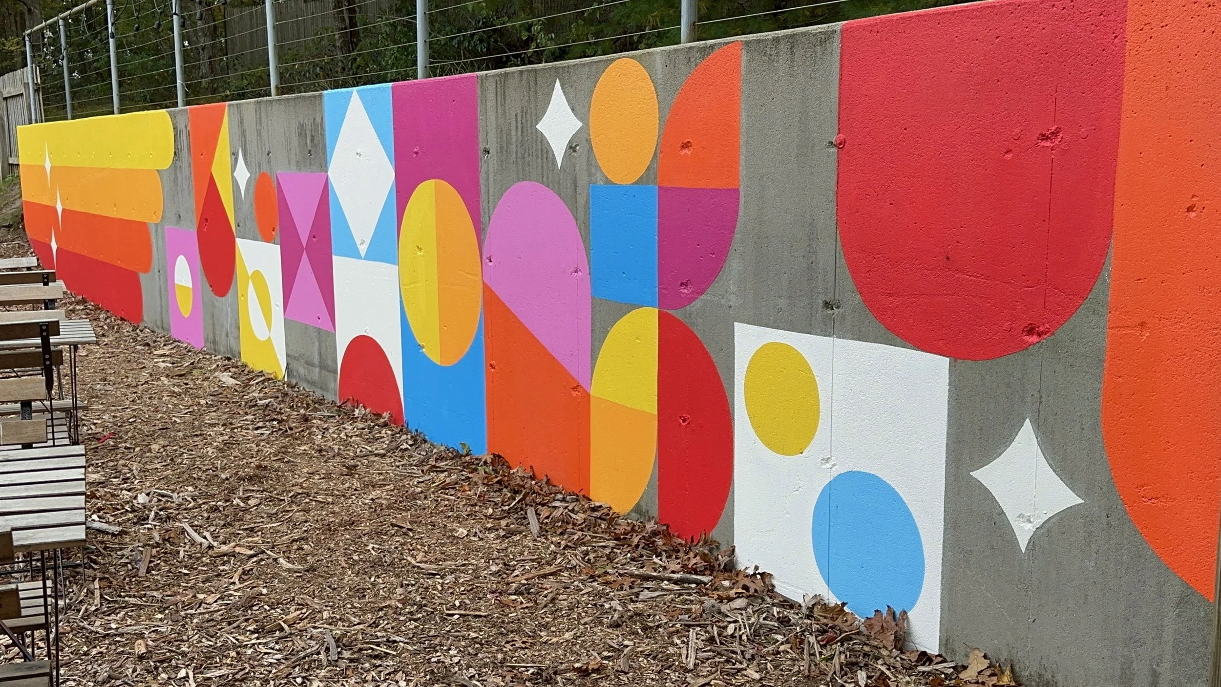 SHINE Studio Retaining Wall: a bright, geometric installation transformed this concrete retaining wall to a cheerful backdrop to the outdoor seating and playground areas.  One of a number of mural installations commissioned by the Studio of local art