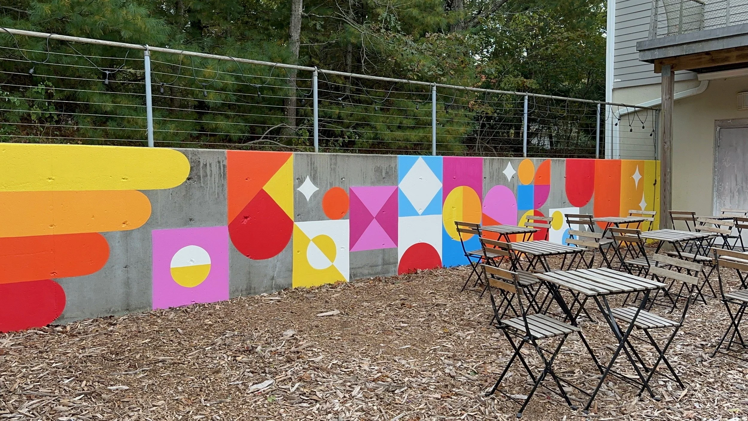 SHINE Studio Retaining Wall: a bright, geometric installation transformed this concrete retaining wall to a cheerful backdrop to the outdoor seating and playground areas.  One of a number of mural installations commissioned by the Studio of local art