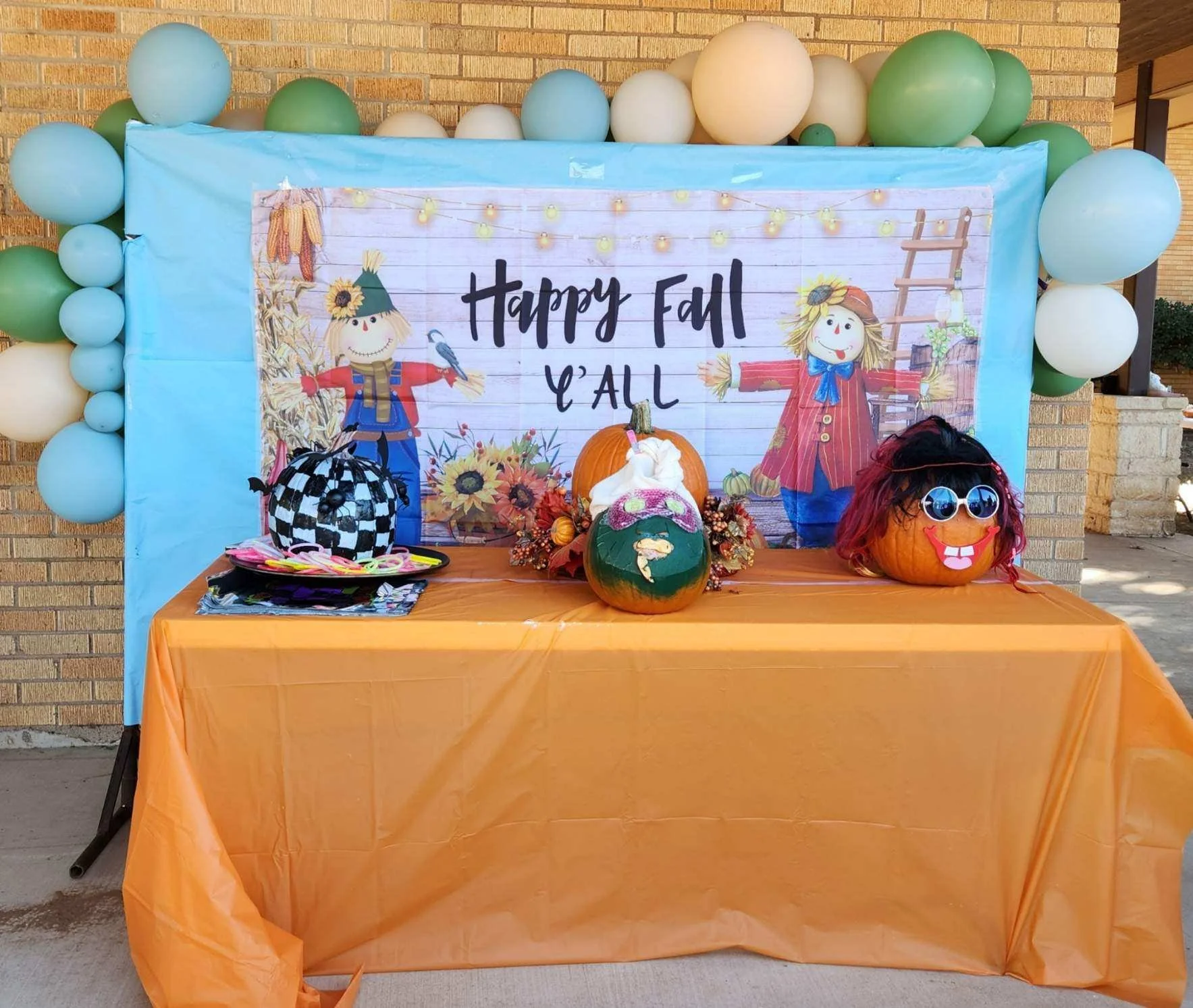 Fall-themed display with pumpkins decorated as characters, a seasonal backdrop, and colorful balloons.