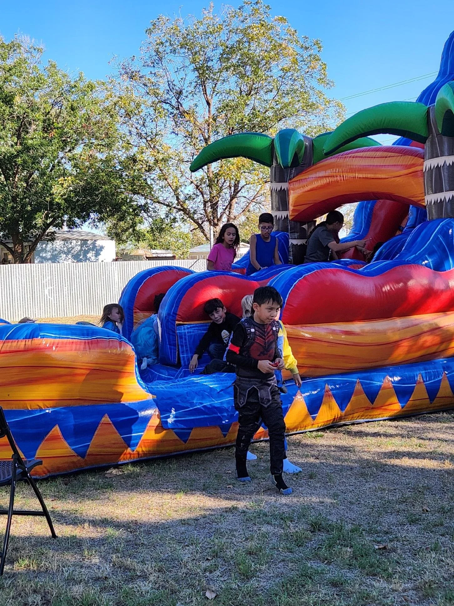 Children playing on a colorful inflatable water slide outdoors on a sunny day.