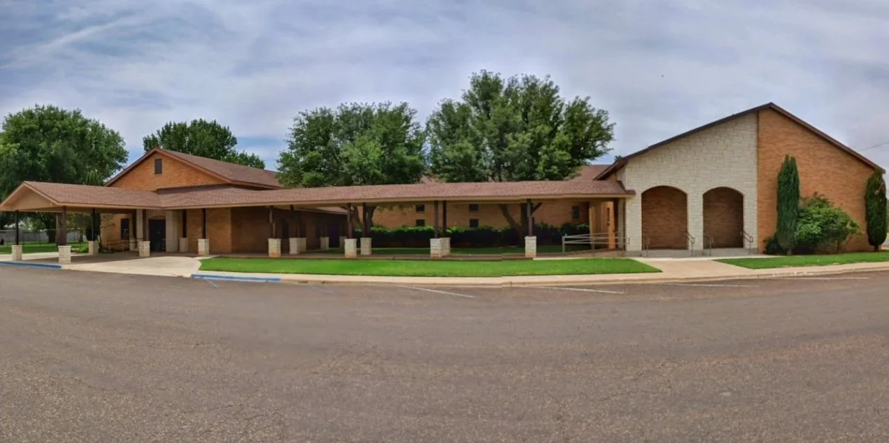 A single-story brick building with a covered entrance, landscaping, and parking area, possibly a church or community center.