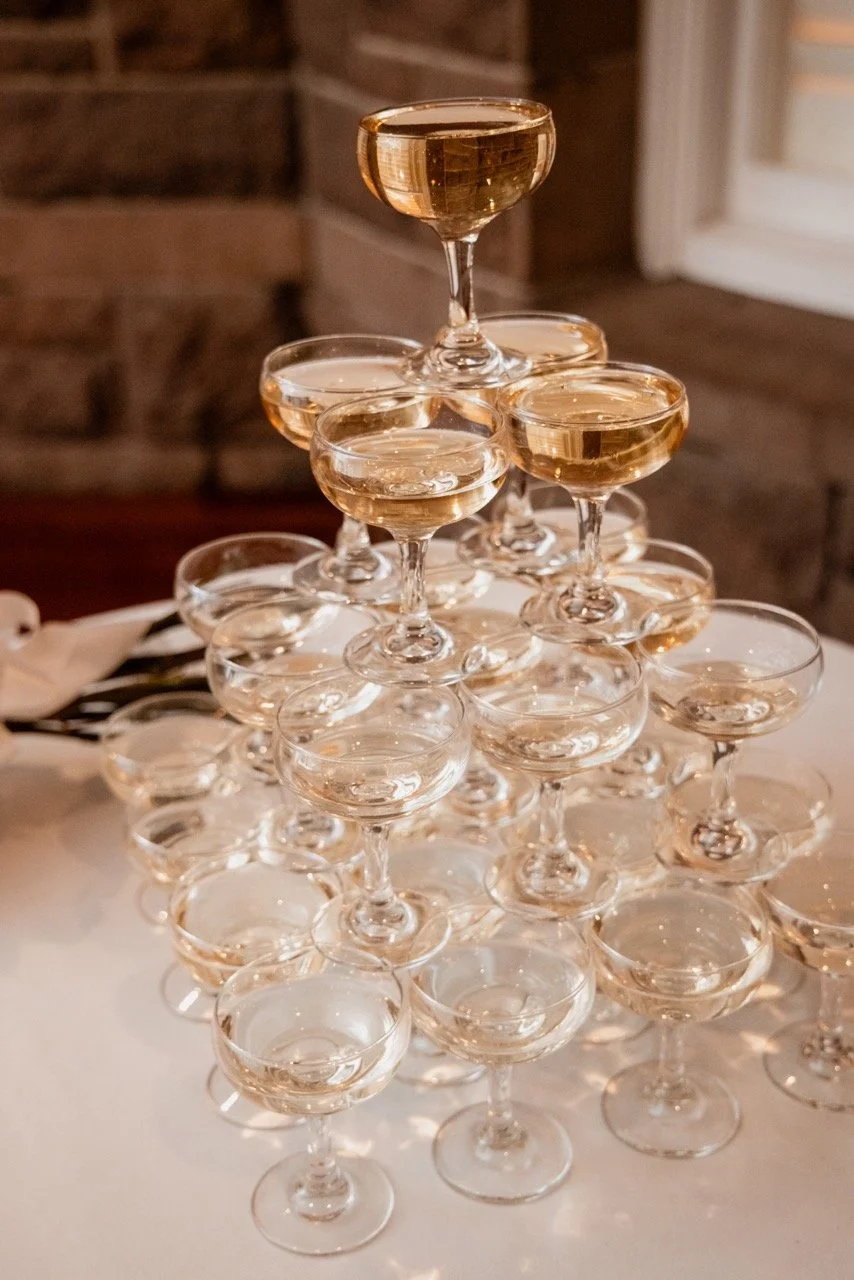 A pyramid of champagne glasses filled with champagne, set on a white tablecloth in a cozy setting.