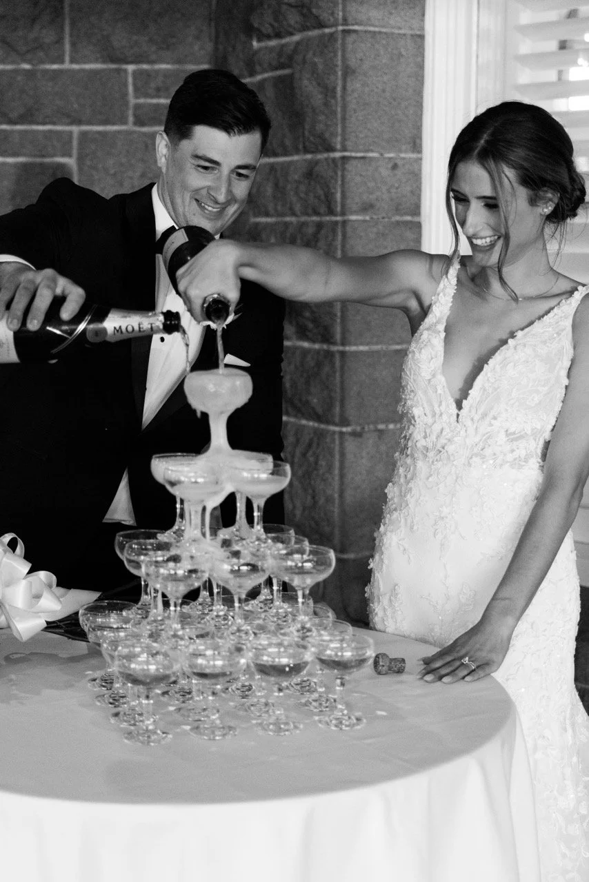 A bride and groom pouring champagne into a pyramid of glasses at their wedding reception.