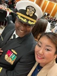 Person in a military uniform and hat taking a selfie with a woman in an indoor setting.