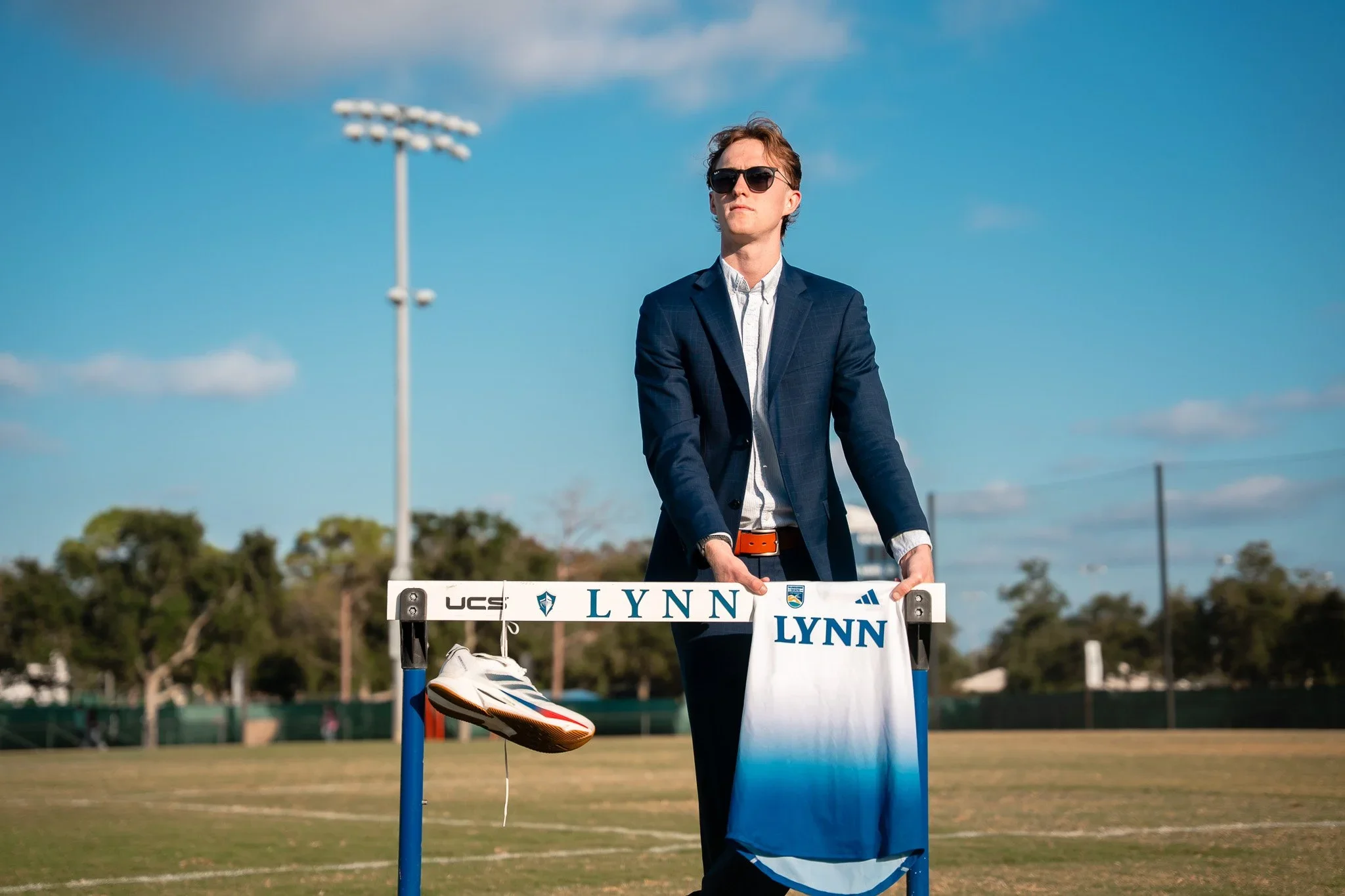 Lynn University student-athlete Cameron posing with a hurdle, running shoe and team jersey