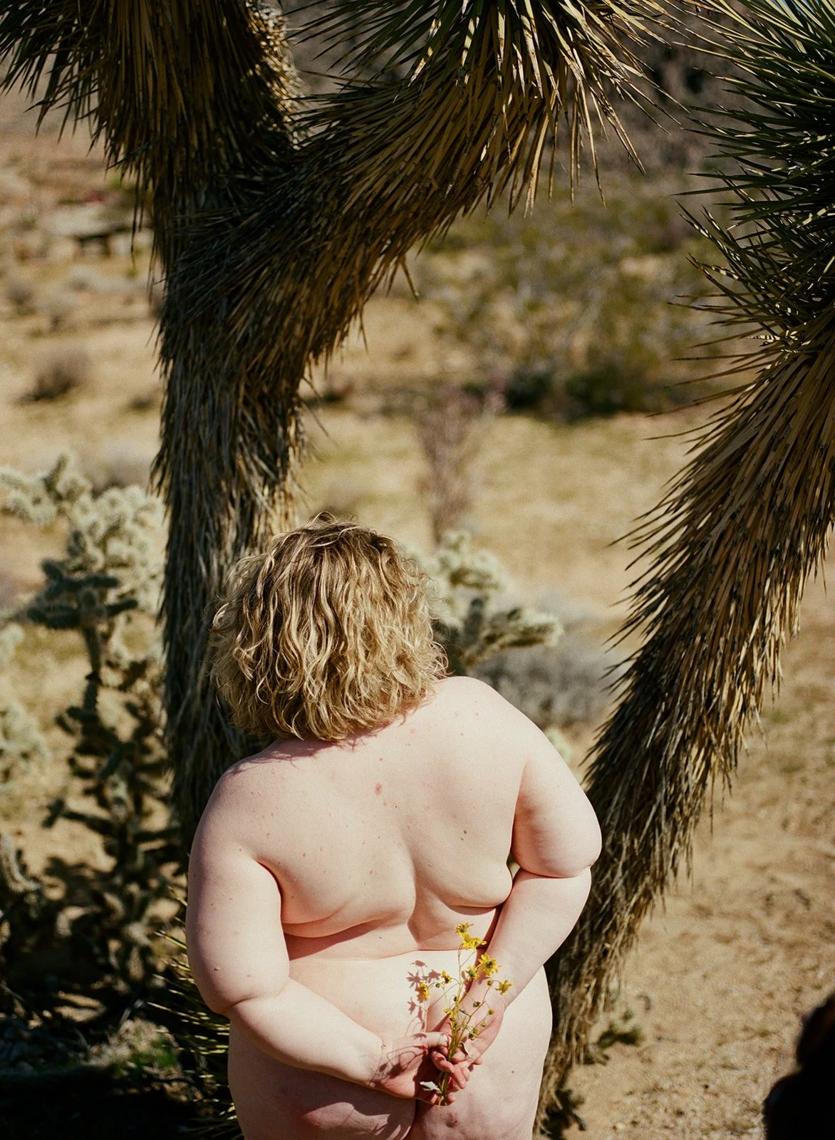 nude woman holds yellow flowers behind her back in the desert landscape
