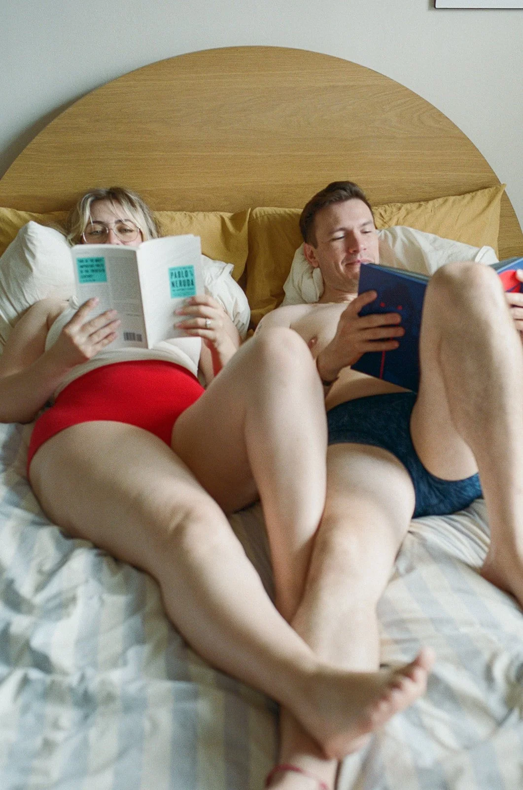 Couple laying in bed in their underwear reading books 