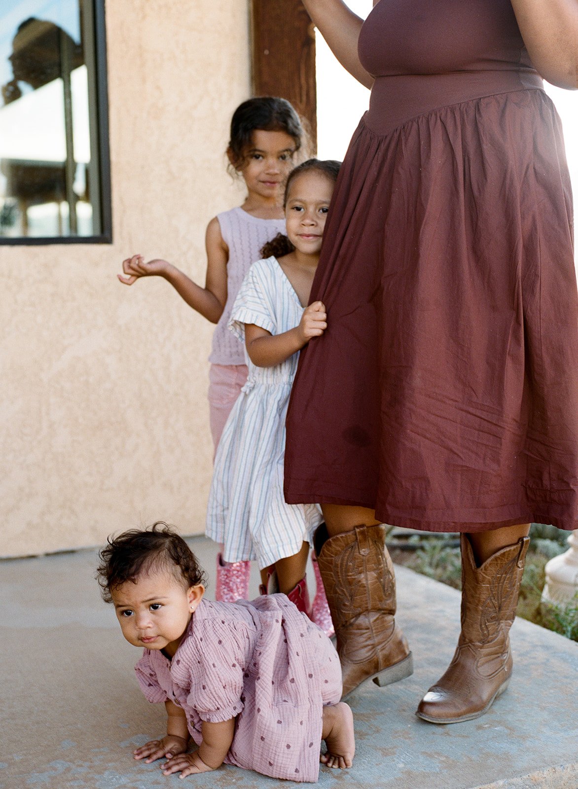 two children stand beside their mother and a toddler is on the ground in front of them