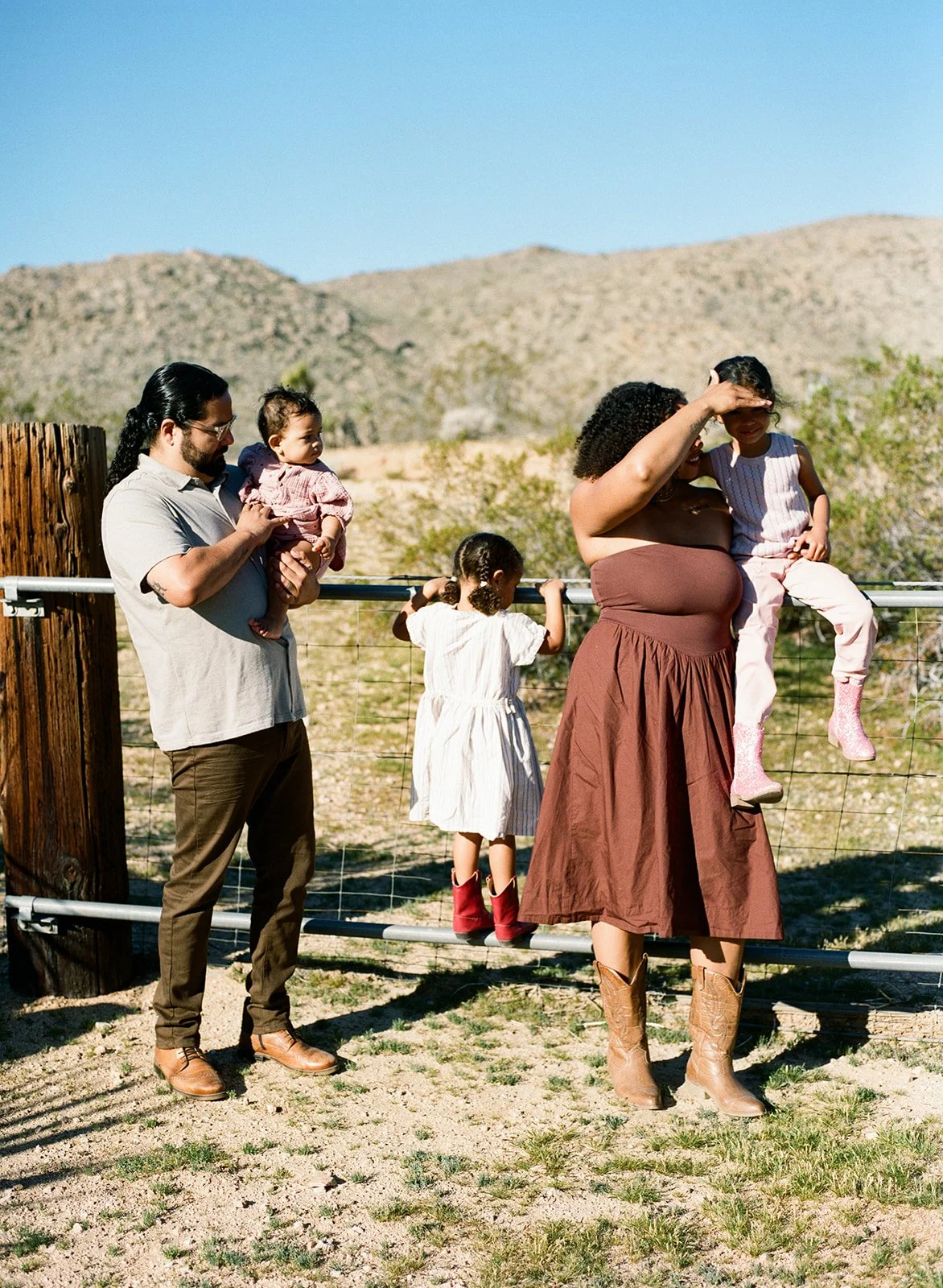 a family of five stands on and in front of a metal gate at joshua tree