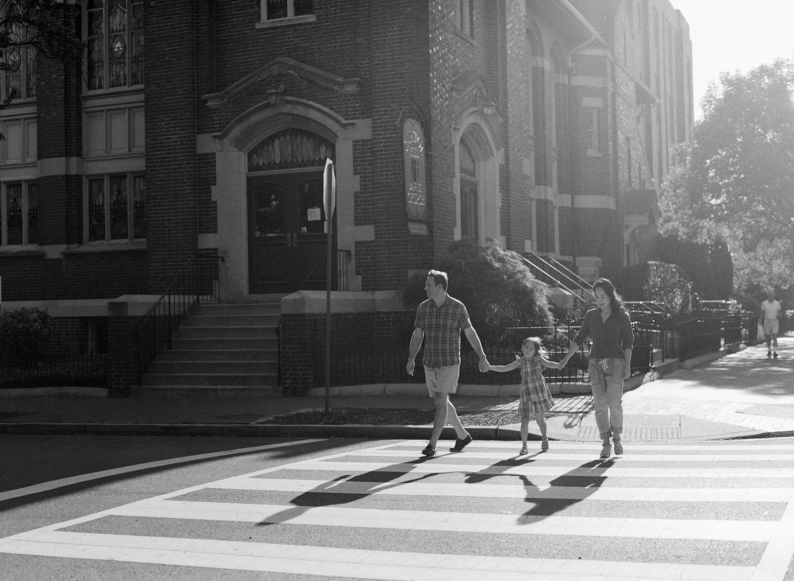 Parents hold hands with young girl while crossing the street during a Washington DC family photo session 