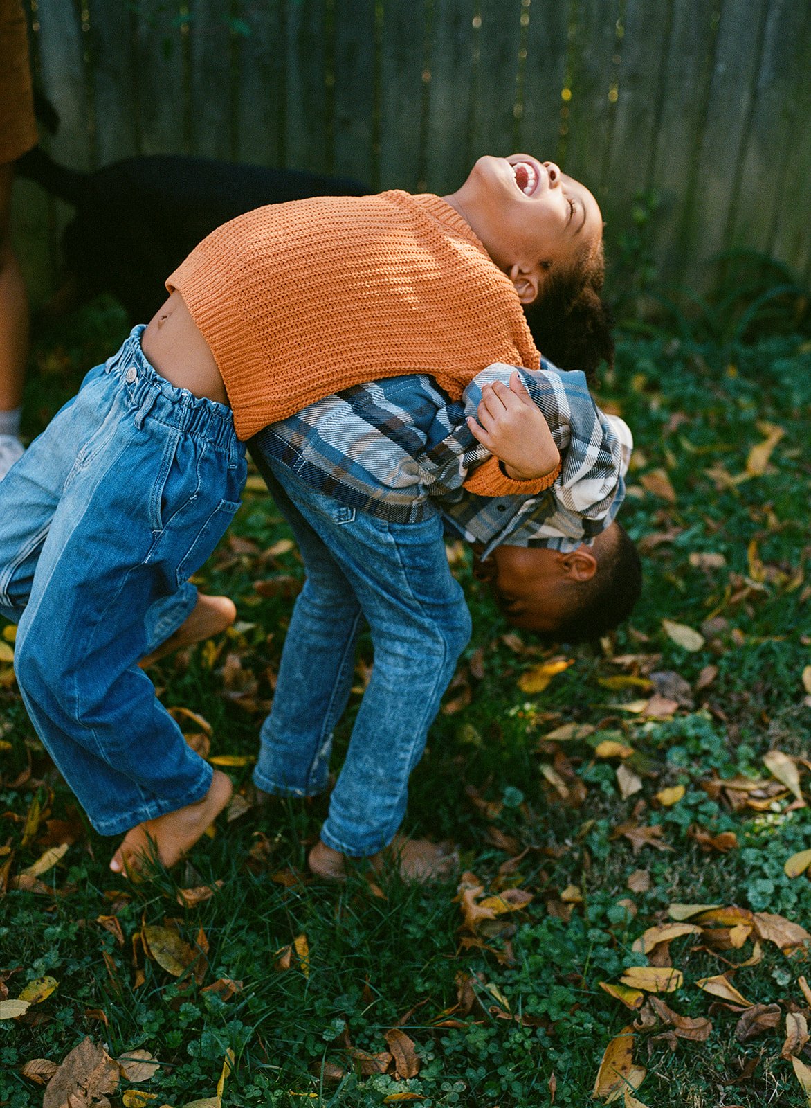 siblings playing in the backyard while a brother tries to pick up his sister on his back and she is laughing 