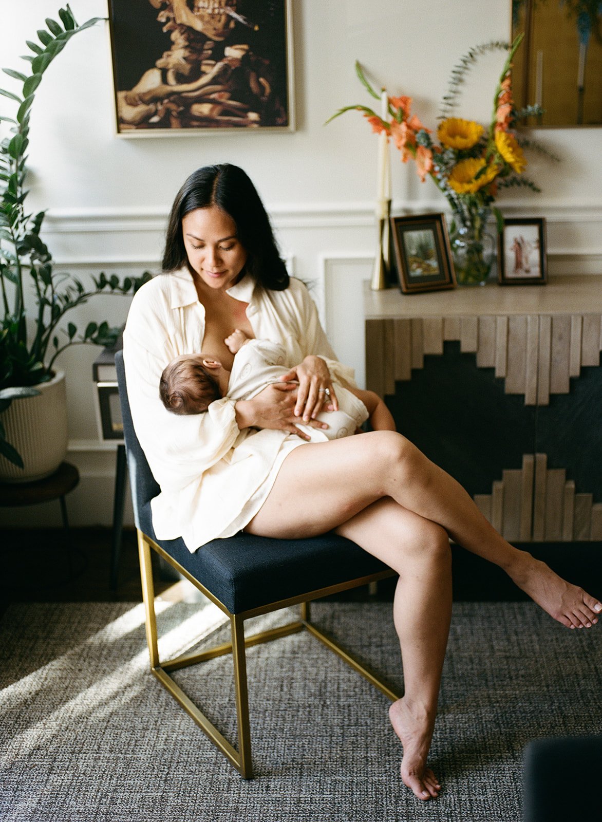 A mother looks down at her child while nursing during a newborn photography session in her home 
