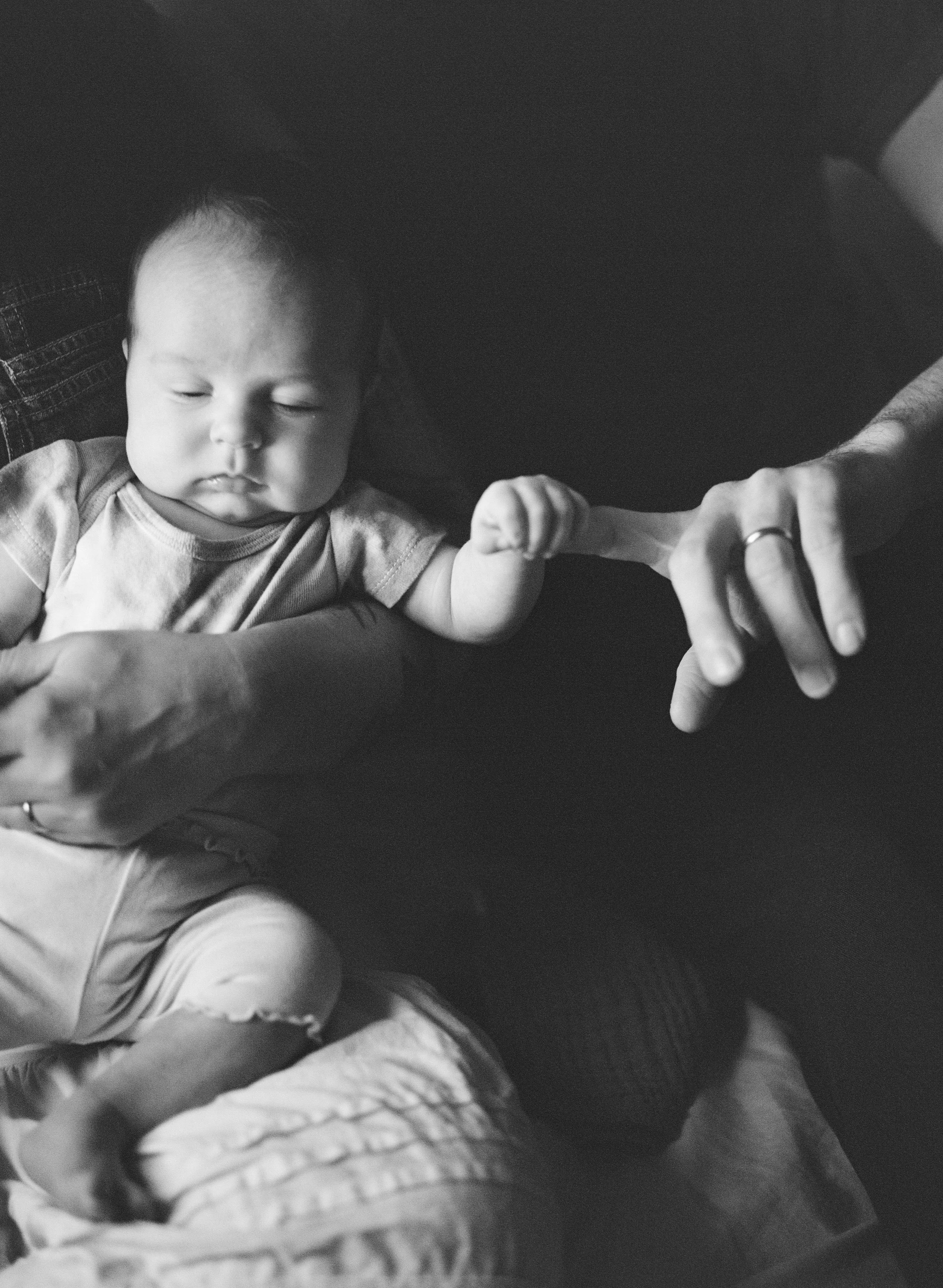 Sleeping infant holds the finger of their parent in a black and white film photograph from their newborn photography session. 