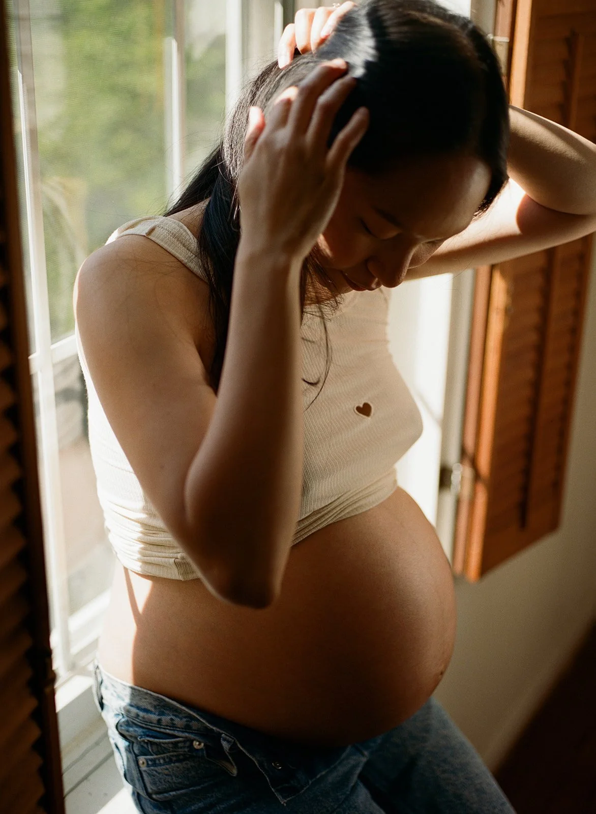 pregnant mother fixes her hair while she perches on the window sill 