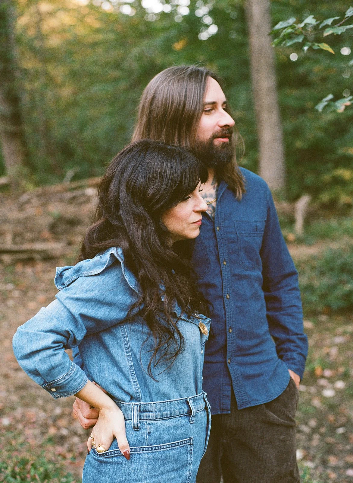 A woman and man stand together wearing denim button down tops and looking off camera 