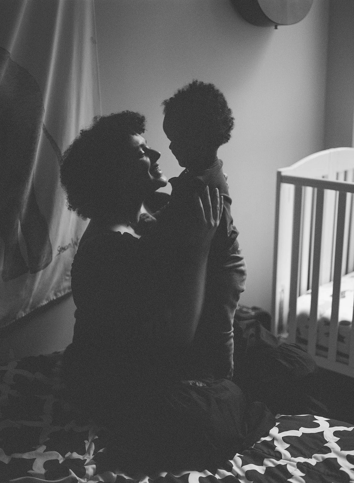 black and white image on film shows the silhouette of a mother holding her toddler in the child's room 
