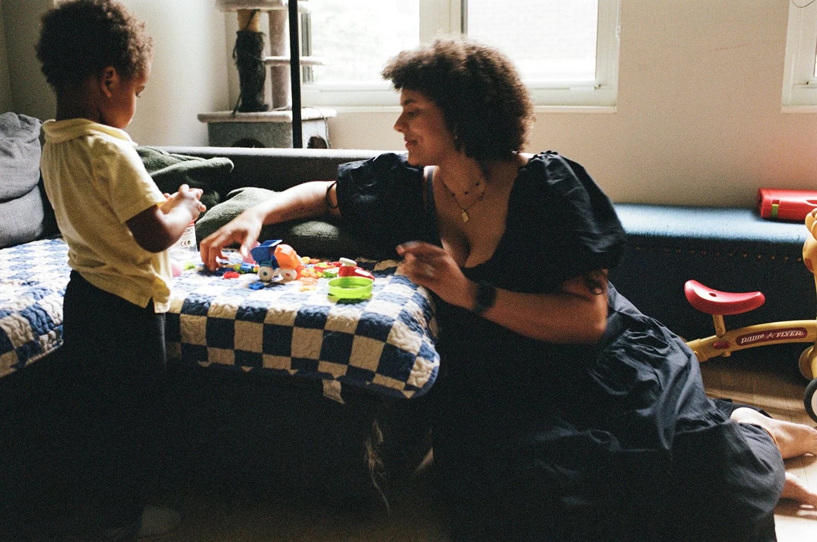 a mother sits on the floor illuminated from behind by window light while she plays with her toddler