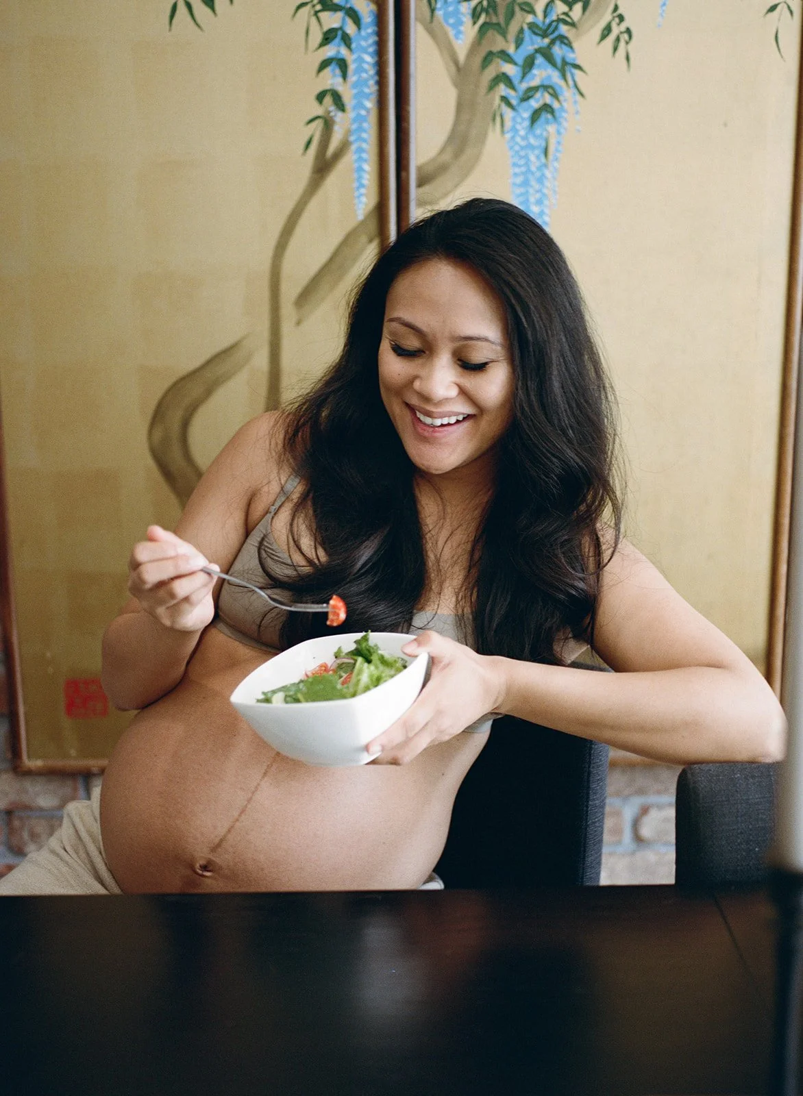 pregnant mother sits at the table while eating a bowl of salad 