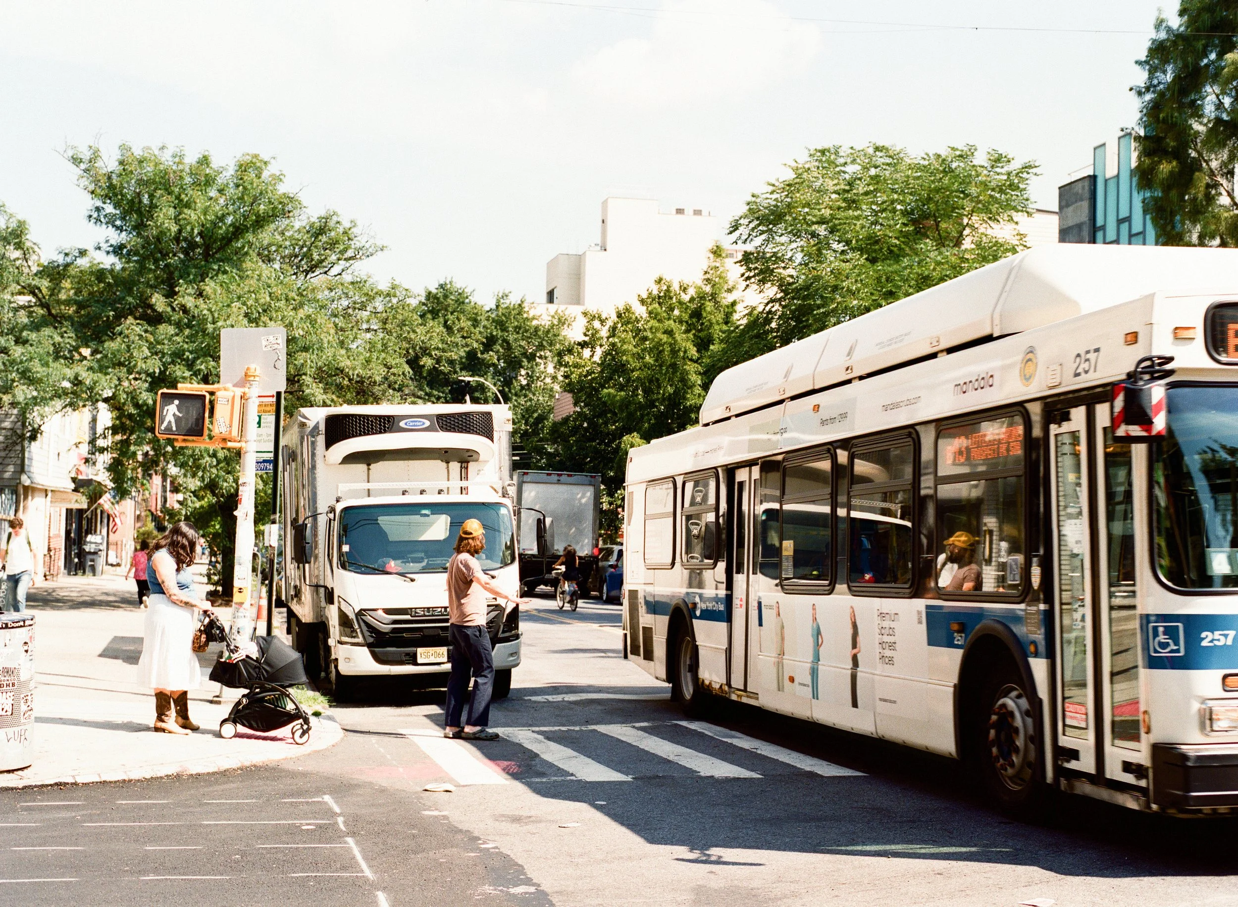 A couple crosses the street in NYC as a bus crosses the intersection in front of them. 