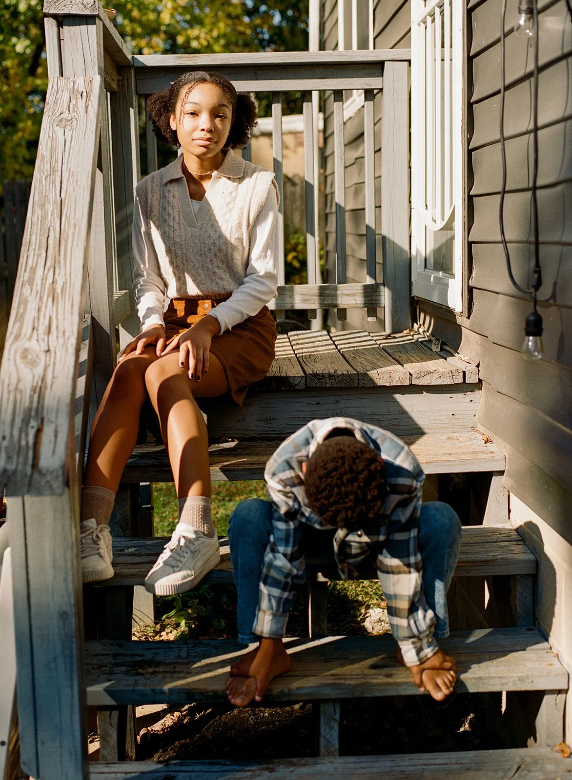 a pair of siblings sit on their back porch taking a break from their family photo session in the backyard 
