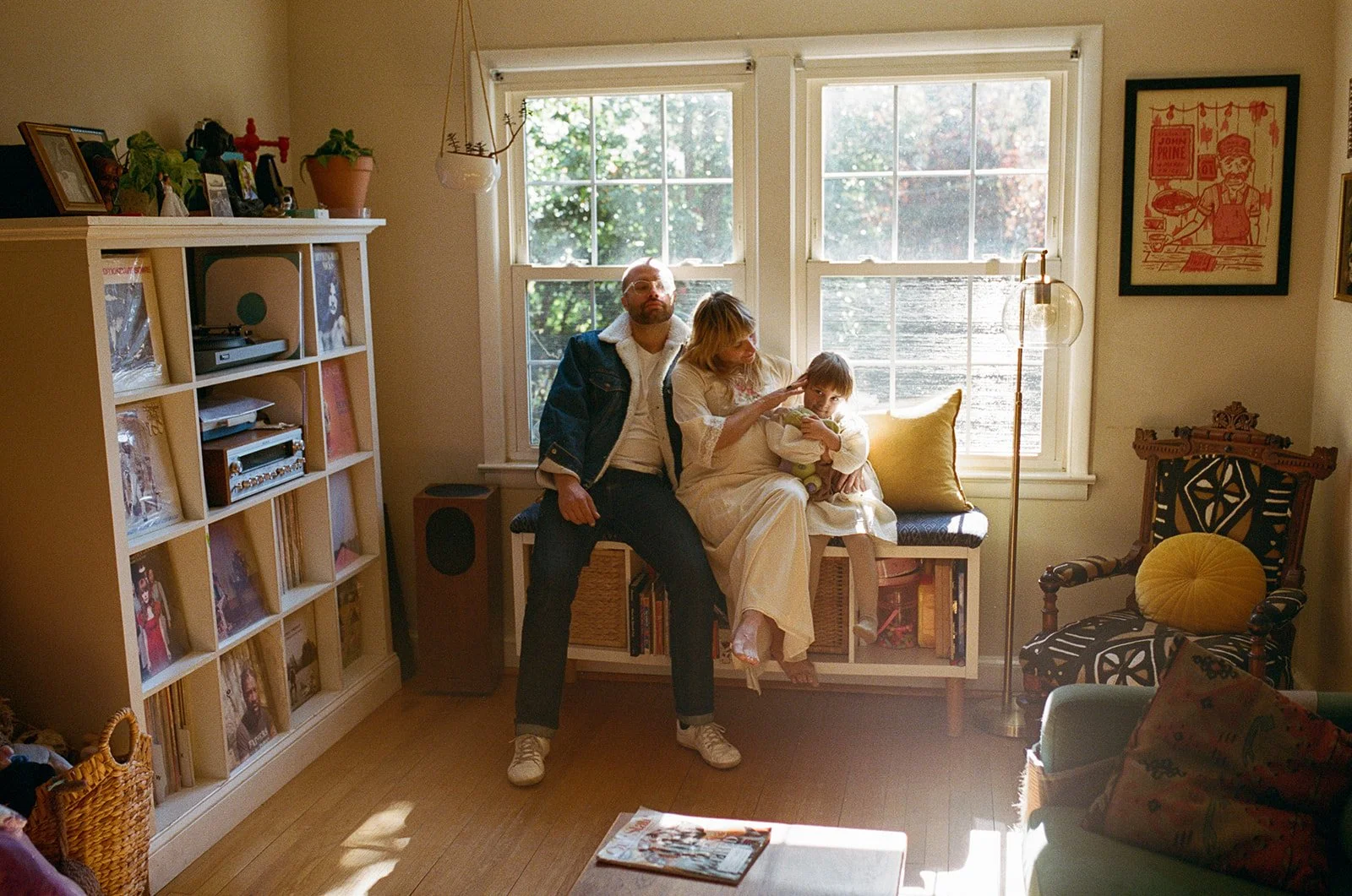 family sits on a bench in the living room window while mom plays with her daughters hair during a family photography session 
