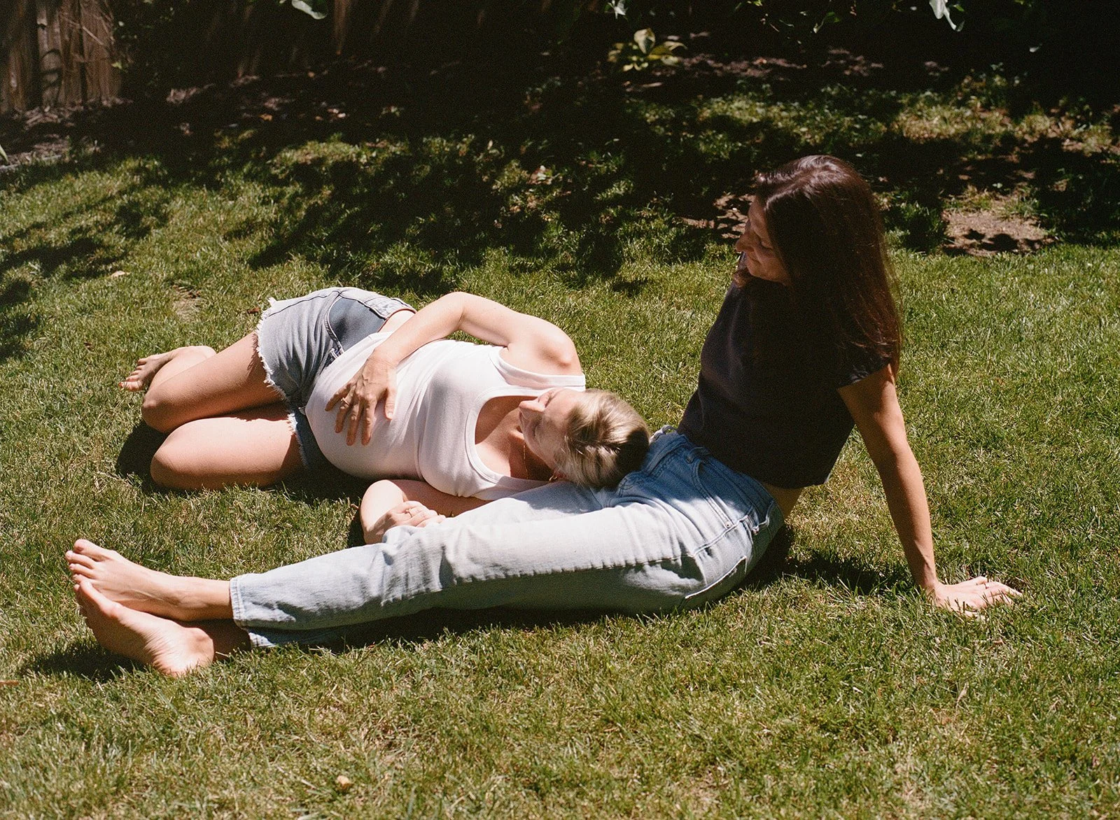 Two expectant moms sitting in the yard together during a maternity session on film 