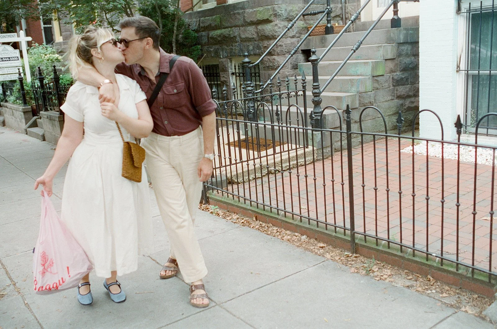 A man and woman walking down a Washington DC neighborhood sidewalk pause for a kiss 