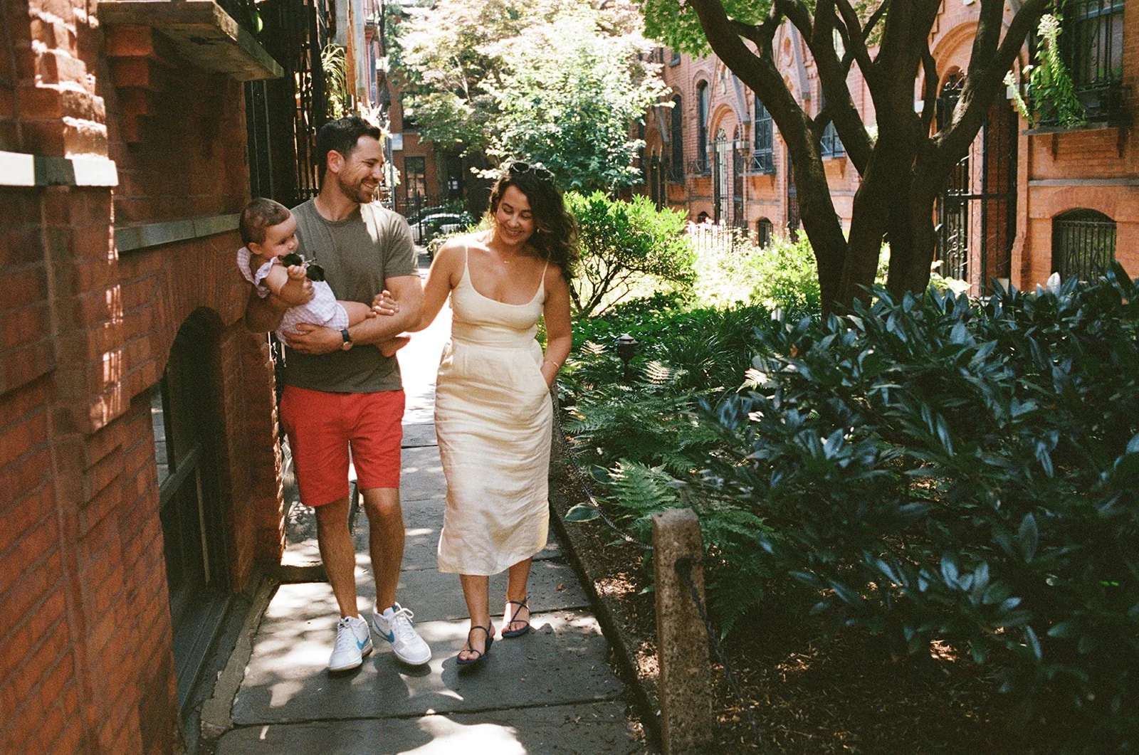 A couple walk arm in arm carrying their infant child during a family photo session in NYC.